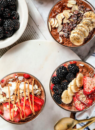 image of three bowls of strawberry overnight oats garnished with various fruit, yogurt, berries and sliced bananas