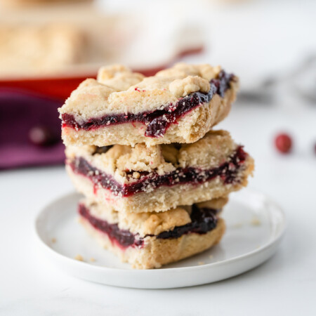 Image of a stack of rich, buttery cranberry shortbread bars filled with tart cranberry sauce on a white plate