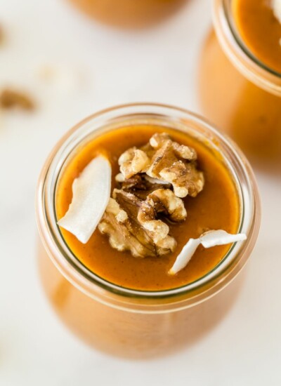 overhead photo of a jar of pumpkin pudding that is sweetened with honey garnished with coconut slivers and toasted walnuts