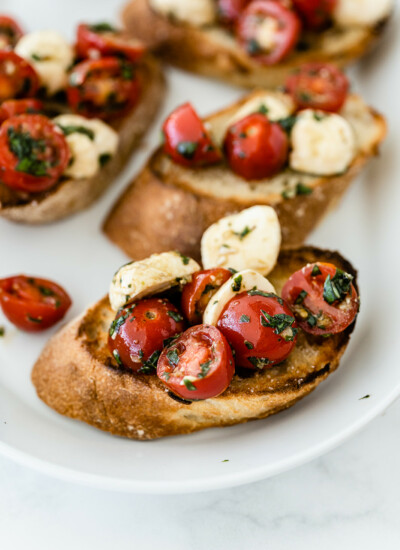 Photo of toasted bruschetta with mozzarella and halved cherry tomatoes with fresh basil and a little oil on a white platter