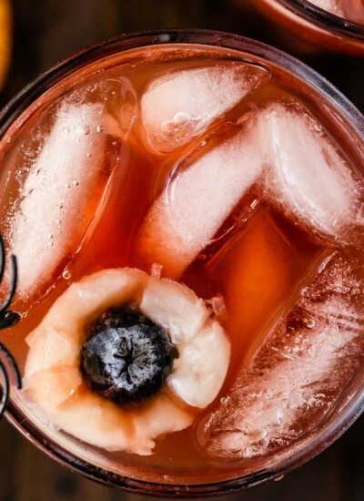 closeup image of a cup of Halloween punch garnished with eyeballs made of fruit Lychees and blueberries with a fake spider on the rim for an extra spooky punch