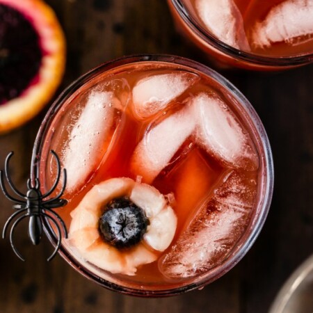 overhead photo of a cup of Halloween punch garnished with eyeballs made of fruit Lychees and blueberries with a fake spider on the rim to look extra spooky