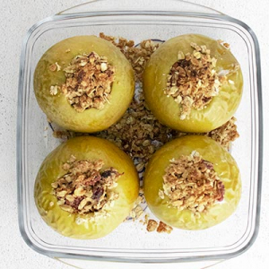 Image of four air fryer baked apples with an oat-based crumble filling inside each apple with cinnamon, raisins and pecans.