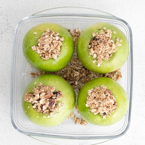 Image of four apples with an oat-based crumble filling inside each apple with cinnamon, raisins and pecans ready to be made in the air fryer.