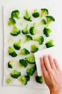 image of a hand patting dry scattered broccoli florets on white parchment paper