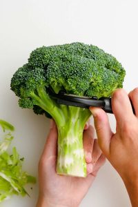 image showing a hand with a potato peeler taking off the skin on the trunk of broccoli