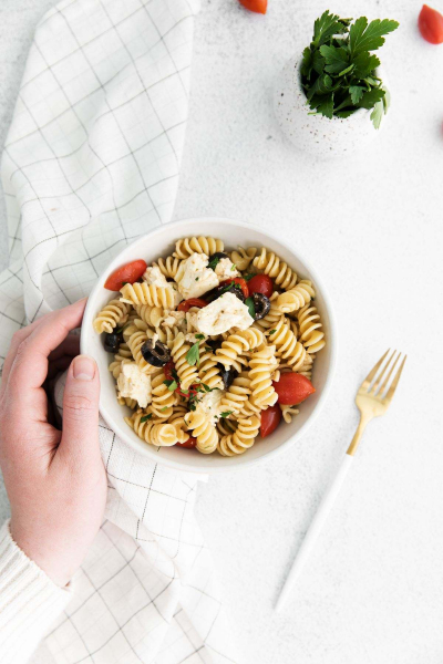 hand hold bowl of greek style pasta salad