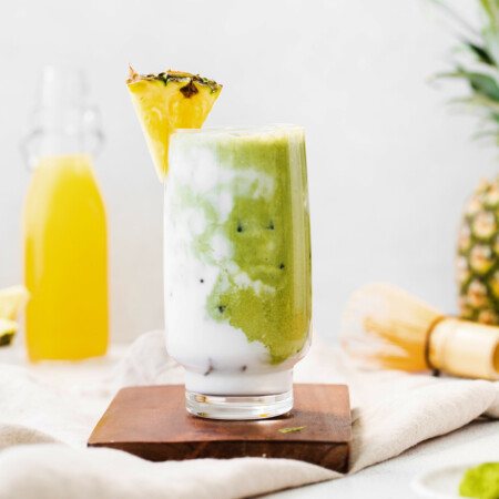 pineapple matcha drink in glass on brown cutting board
