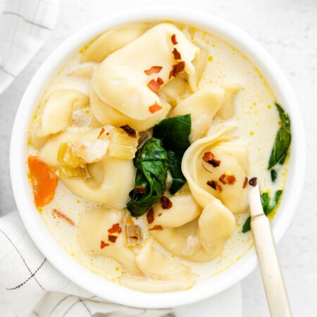 Photo of a bowl of Instant Pot Tortellini Soup that looks super rich and creamy with cheesy tortellini, fresh baby spinach, and carrots and garnished with a sprinkle of red pepper flakes