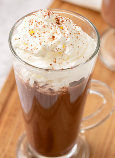 Image of a glass full of Instant Pot Hot Chocolate topped with whipped cream and dusted with cocoa powder and it looks super rich and chocolaty