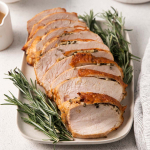 Image of sliced Air Fryer Turkey Breast on a platter that looks moist, golden-brown and garnished with fresh rosemary sprigs