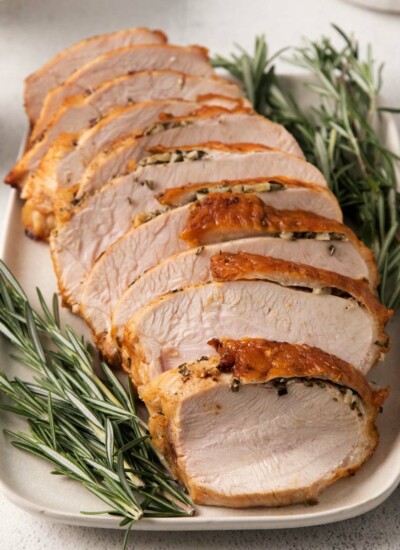 Image of sliced Air Fryer Turkey Breast on a platter that looks moist, golden-brown and garnished with fresh rosemary sprigs