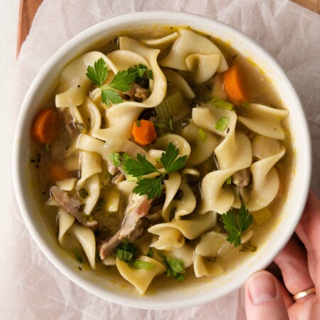 top view image of a bowl of hearty Instant Pot Turkey Soup loaded with veggies, noodles, and carrots with a pop of flavor from garlic and sage.
