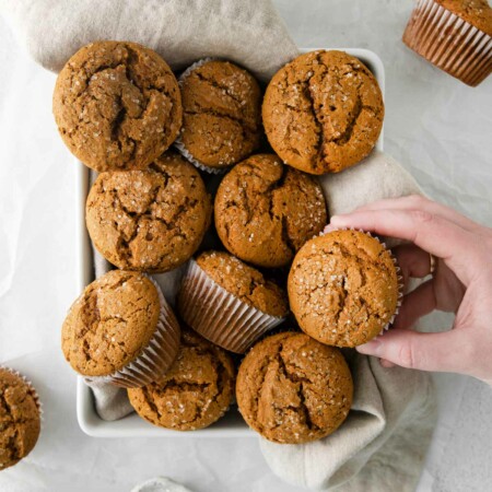 Image shows a hand grabbing a gingerbread muffin out of a pan full