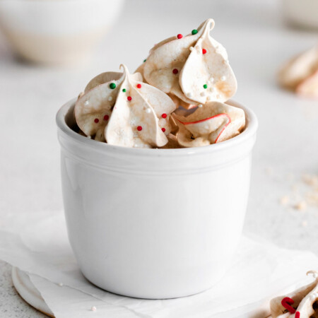 Image of a cup full of red and green speckled peppermint meringues that are light and airy, melt-in-your-mouth swirls of peppermint.