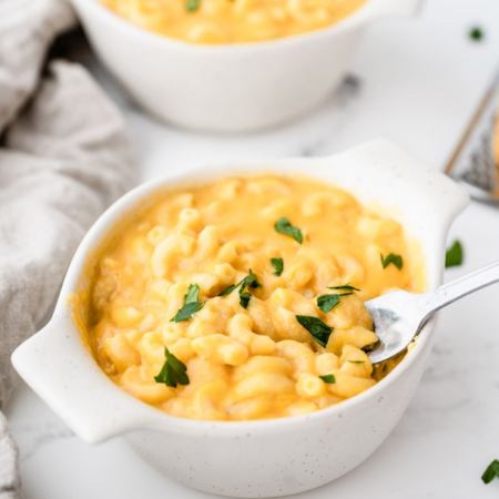 image of a white bowl full of creamy sweet potato mac and cheese garnished with parsley and a spoon dipping into the dish
