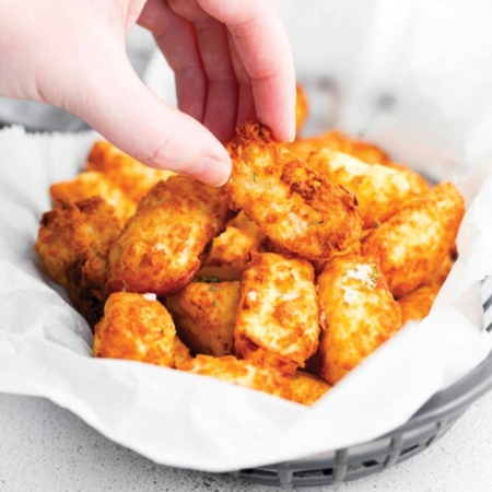 Air fryer recipe for tater tots nice and crispy with a hand reaching for one