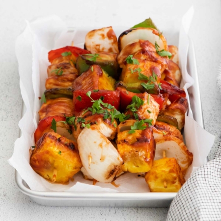 image of chicken pineapple kabobs on a white tray with layered chicken pineapple onion red and green bell peppers and garnished with parsley