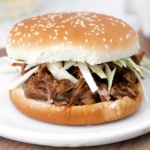 image of an instant pot pork shoulder sandwich showing perfectly seasoned pork shoulder on a hamburger bun garnished with raw cut green cabbage on a white plate