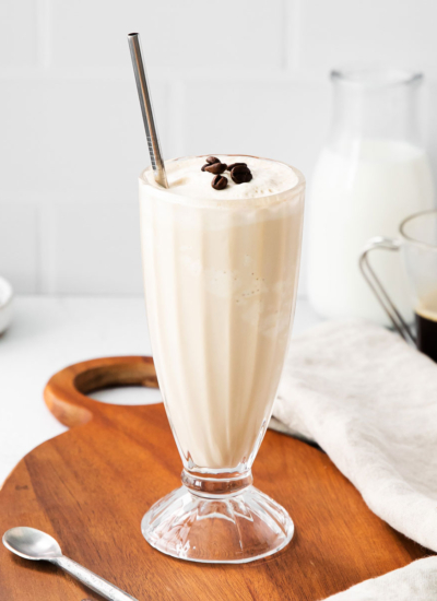 side view image of a tall glass of a creamy mocha milkshake garnished with roasted espresso beans and a silver straw