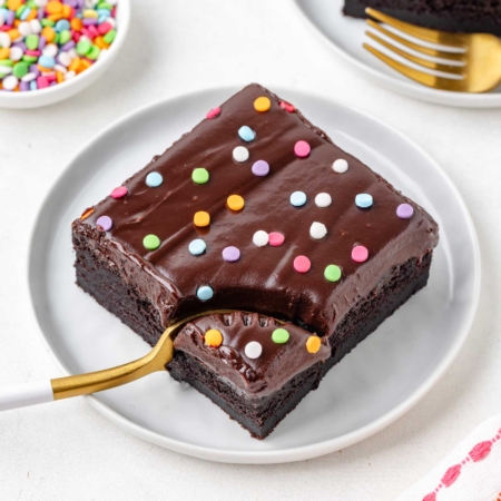 fork digging into a slice of a brownie with ganache on top on a white plate