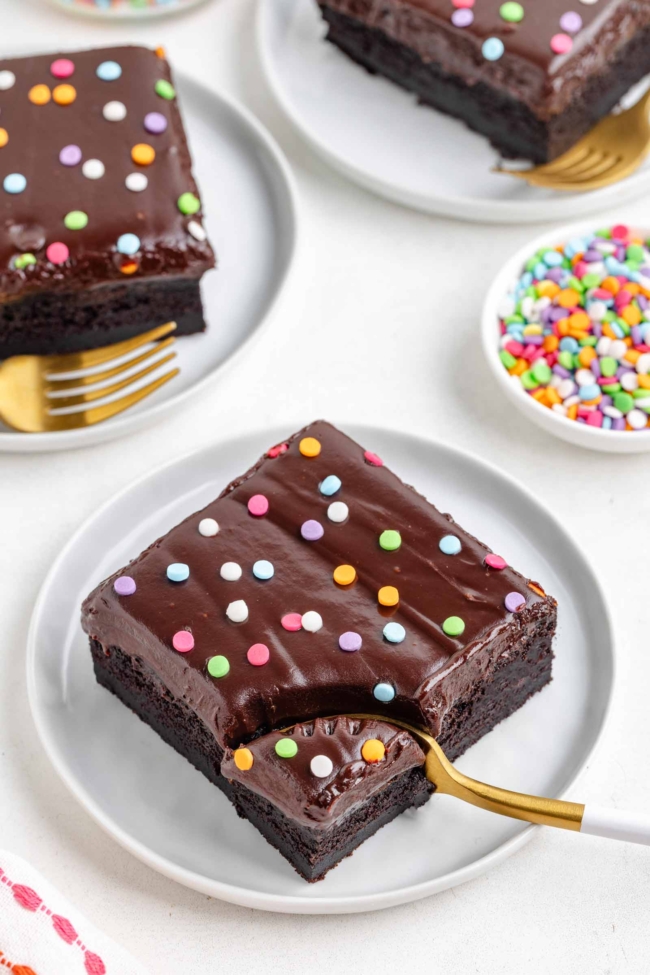 a brownie with ganache on a white plate with a fork digging into it