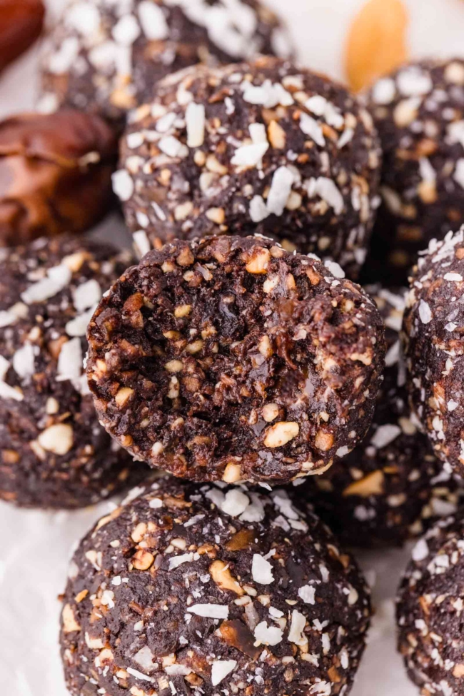 close-up of a stack of chocolate coconut nut balls on a white plate with some cashew in background