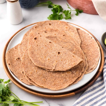 white plated filled with whole wheat tortillas with tortilla warmer in background