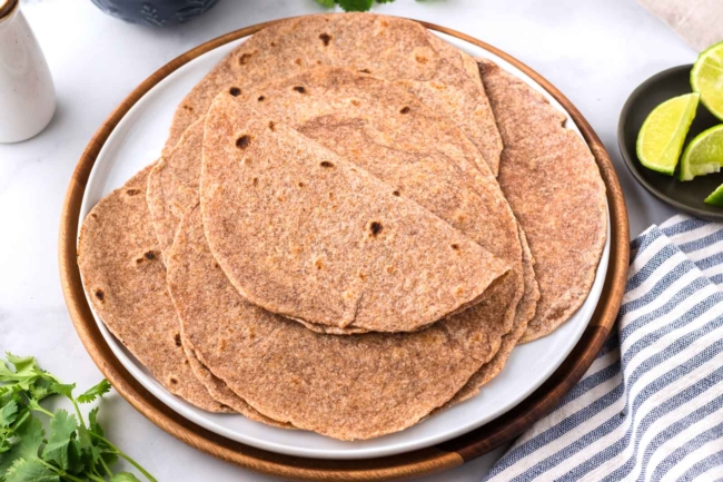 stack of whole wheat tortillas on a white plate with a napkin under plate