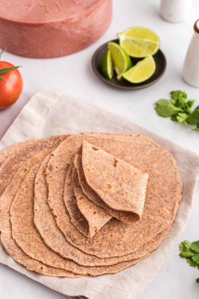 stack of whole wheat tortillas folded in a way to show how pliable they are, on a white table