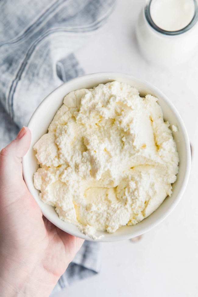 hand holding a bowl of freshly made ricotta cheese