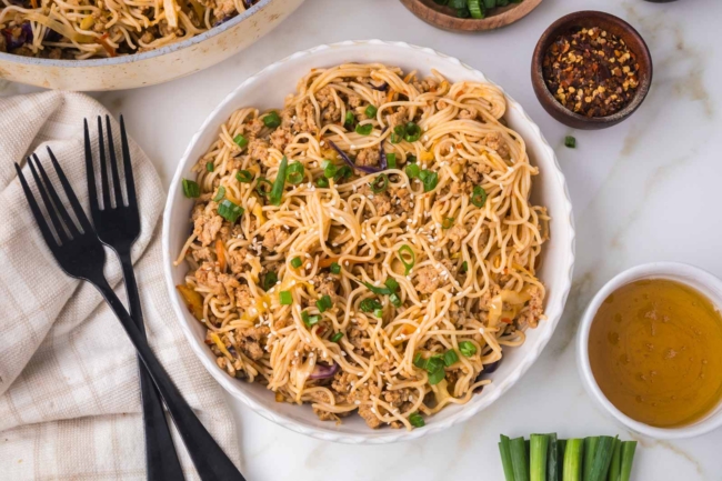 white bowl filled with honey garlic noodles on a white table with a fork on the side