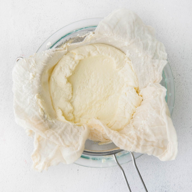fresh ricotta being strained using a cheesecloth