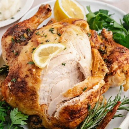 close-up of oven roasted whole chicken on a serving dish, partially cut into