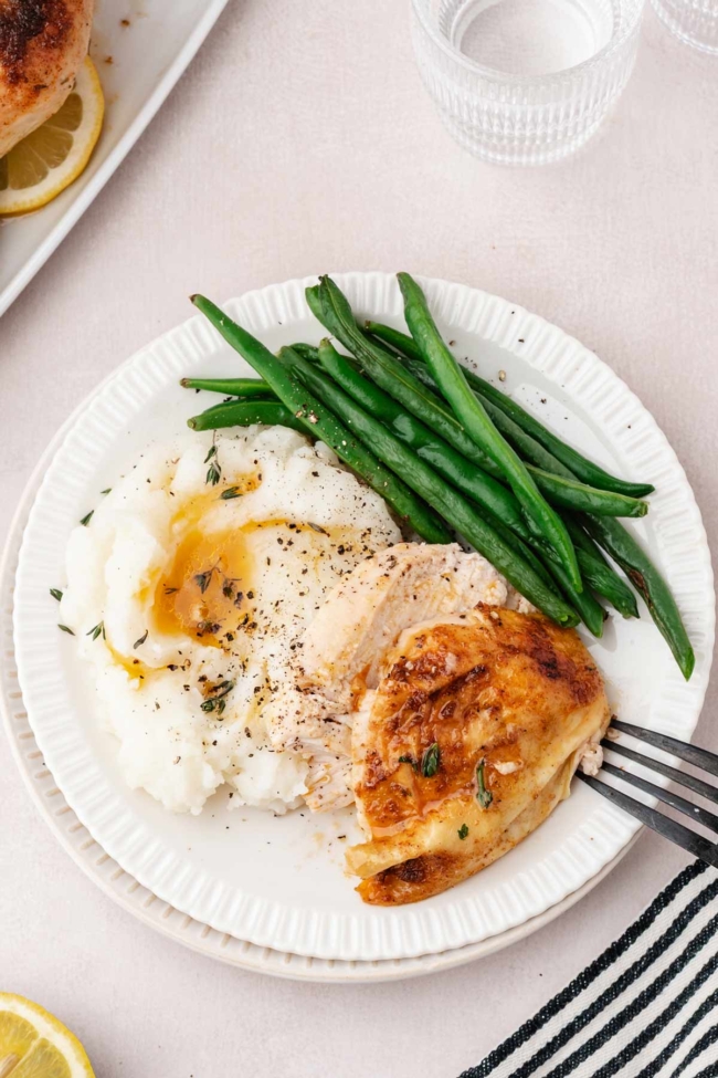 sliced chicken on a white plate with mashed potatoes and green beans