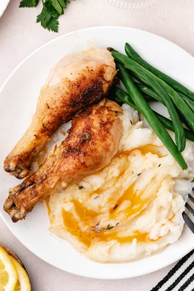 pieces of chicken on a white plate with mashed potatoes and green beans