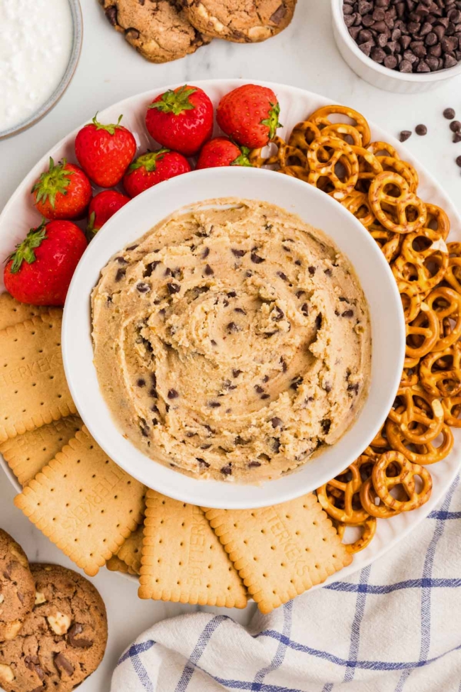 white plate with cookies, strawberries and pretzels and a white bowl of cottage cheese cookie dough