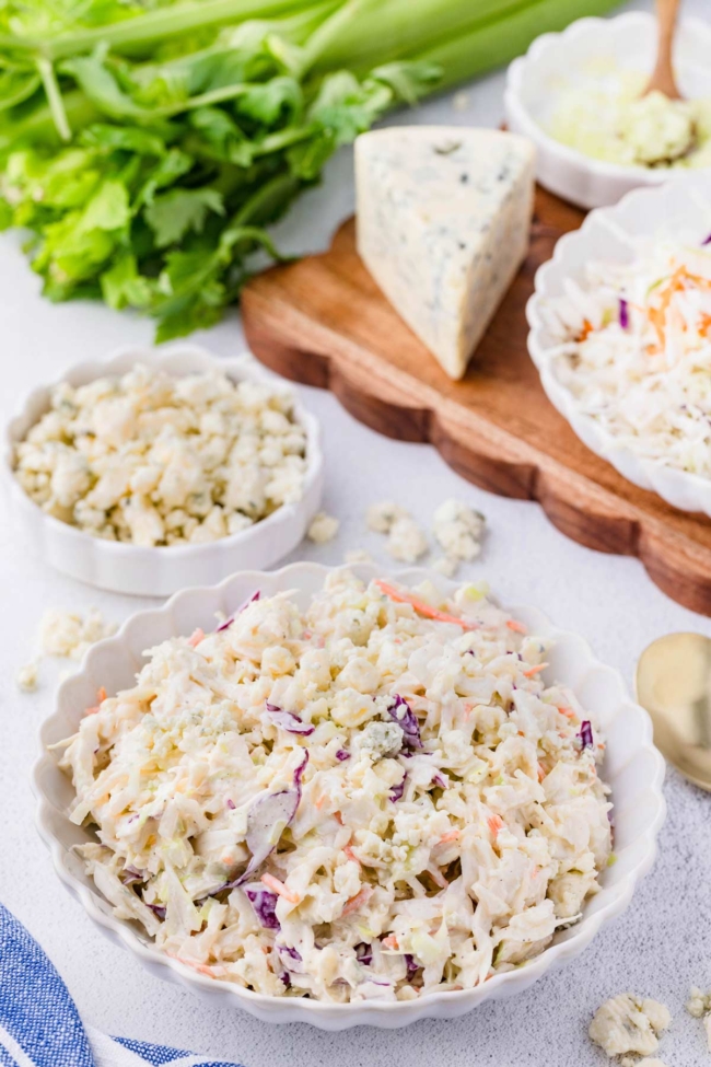 blue cheese slaw in a white bowl with more blue cheese in the background together with the other ingredients