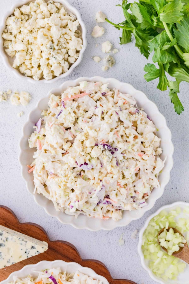 blue cheese coleslaw in a white plate on a white table with celery, parsley and blue cheese in the background