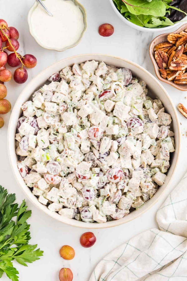 white bowl filled with chicken salad with grapes with more ingredients in background