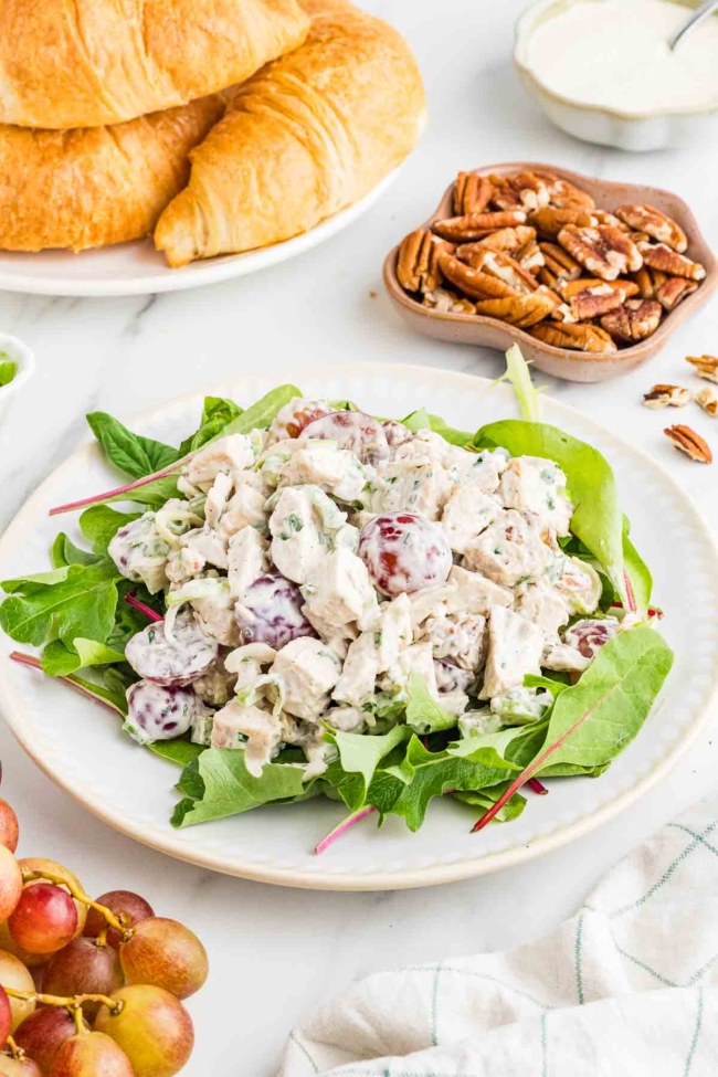 chicken salad with grapes on a bed of lettuce with pecans and croissants in background