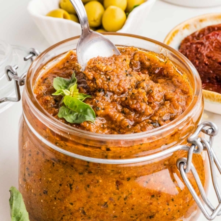 spoon digging into a jar of sun-dried tomato pesto