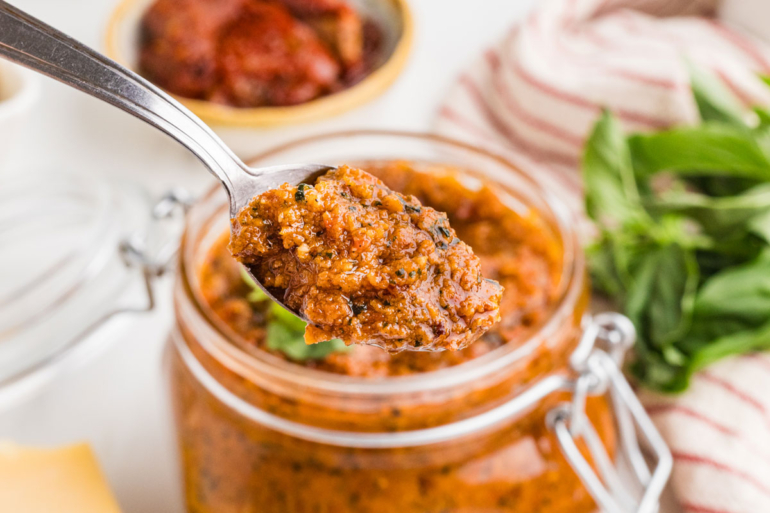 spoon digging into sun-dried tomato pesto in a mason jar