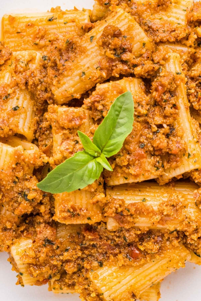 close-up of sun-dried tomato pesto pasta on a white plate with basil on top