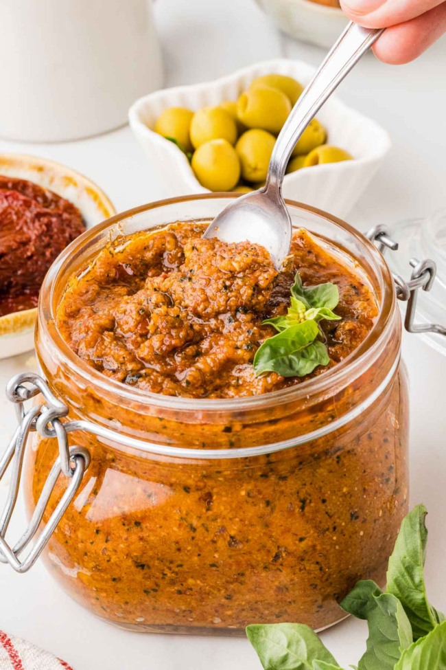 spoon digging into a jar of red pesto