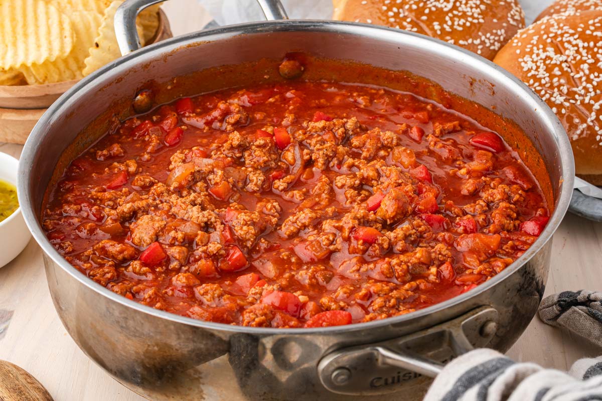 ground turkey sloppy joe filling in a skillet with sandwiches and chips in the background