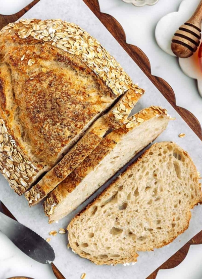 overhead shot of sliced up honey oatmeal sourdough bread on a cutting board with honey in background