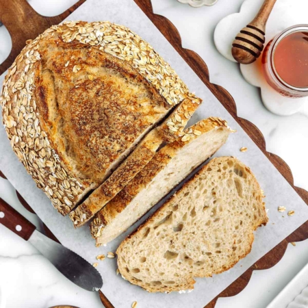 overhead shot of sliced up honey oatmeal sourdough bread on a cutting board with honey in background