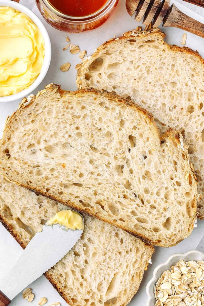 close-up overhead shot of a slice of oatmeal sourdough on white parchment paper with butter in background