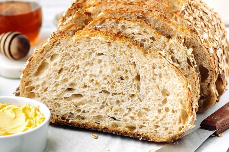 horizontal shot of oatmeal sourdough bread on a cutting board with honey in background